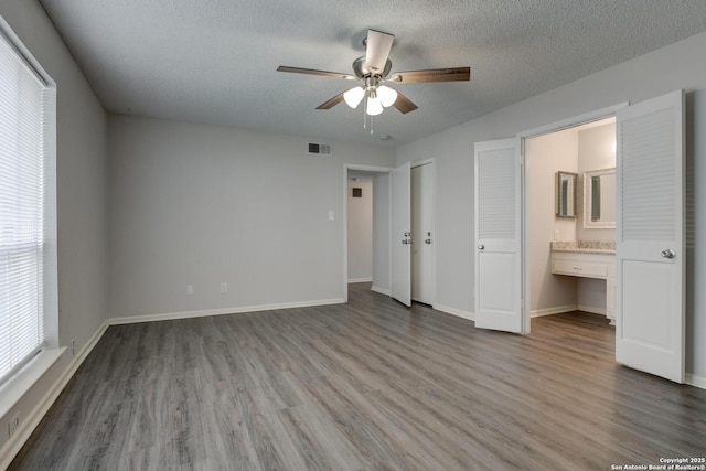 8915 Datapoint Unit 49A, San Antonio, TX 78229 - unfurnished bedroom featuring wood finished floors, baseboards, ensuite bath, a textured ceiling, and a ceiling fan