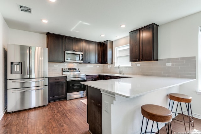 11745 Red Pheasant, San Antonio, TX 78245 - kitchen featuring stainless steel appliances, dark brown cabinetry, a breakfast bar, dark wood-type flooring, and recessed lighting