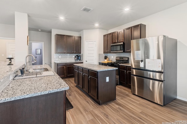 2079 Chelsea Grv, New Braunfels, TX 78130 - kitchen featuring appliances with stainless steel finishes, a sink, dark brown cabinets, light wood-type flooring, and light stone countertops