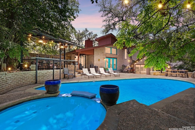 3511 Hunters Cir, San Antonio, TX 78230 - pool at dusk featuring a pool with connected hot tub, a patio area, a fenced backyard, and french doors