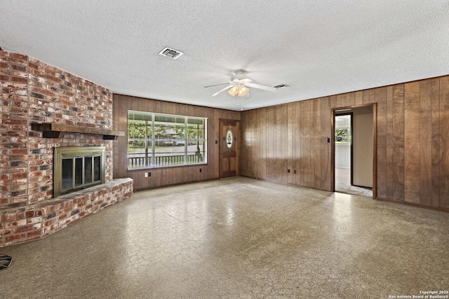 1706 Hickory St, Floresville, TX 78114 - unfurnished living room with wood walls, a ceiling fan, tile patterned floors, a fireplace, and a textured ceiling