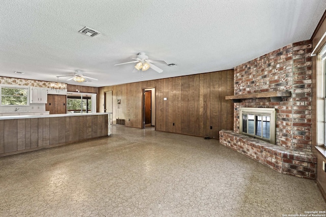 1706 Hickory St, Floresville, TX 78114 - unfurnished living room featuring wood walls, a brick fireplace, ceiling fan, light floors, and a textured ceiling
