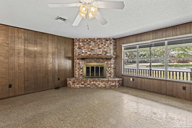 1706 Hickory St, Floresville, TX 78114 - unfurnished living room with wood walls, a ceiling fan, a fireplace, and a textured ceiling