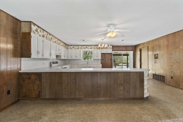 1706 Hickory St, Floresville, TX 78114 - kitchen featuring wooden walls, range, light countertops, a peninsula, and white cabinetry