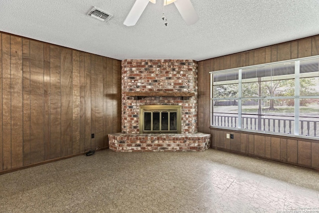 1706 Hickory St, Floresville, TX 78114 - unfurnished living room with wood walls, a ceiling fan, a fireplace, and a textured ceiling