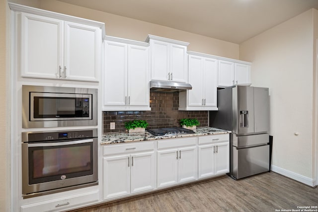 28915 Porch Swing, Boerne, TX 78006 - kitchen featuring stainless steel appliances, under cabinet range hood, decorative backsplash, light wood-type flooring, and light stone counters