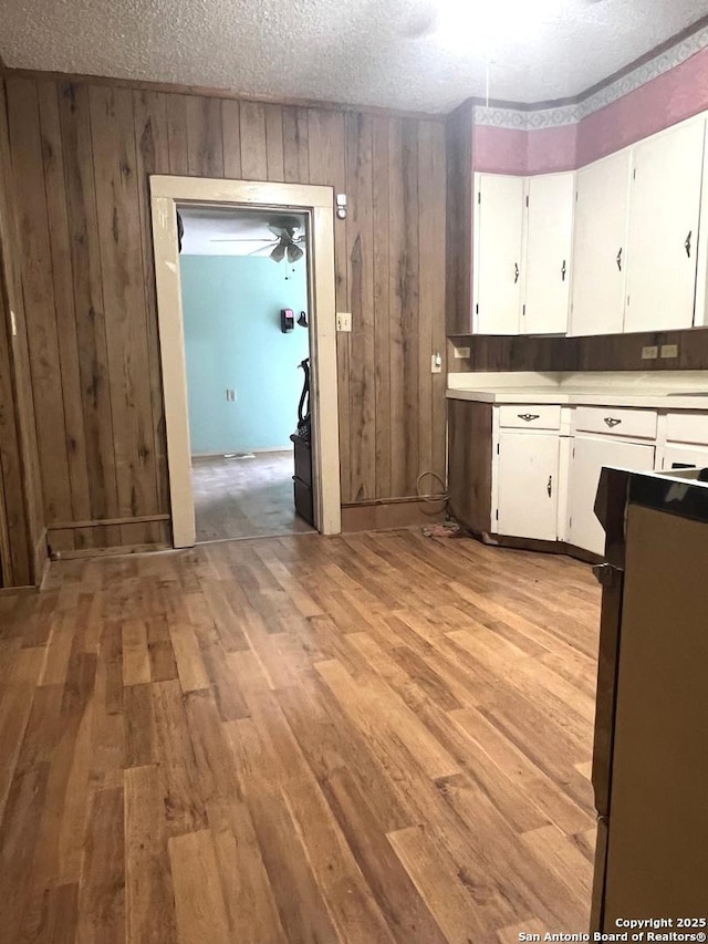 413 4th St, Poteet, TX 78065 - kitchen featuring light countertops, white cabinetry, light wood finished floors, wooden walls, and a textured ceiling