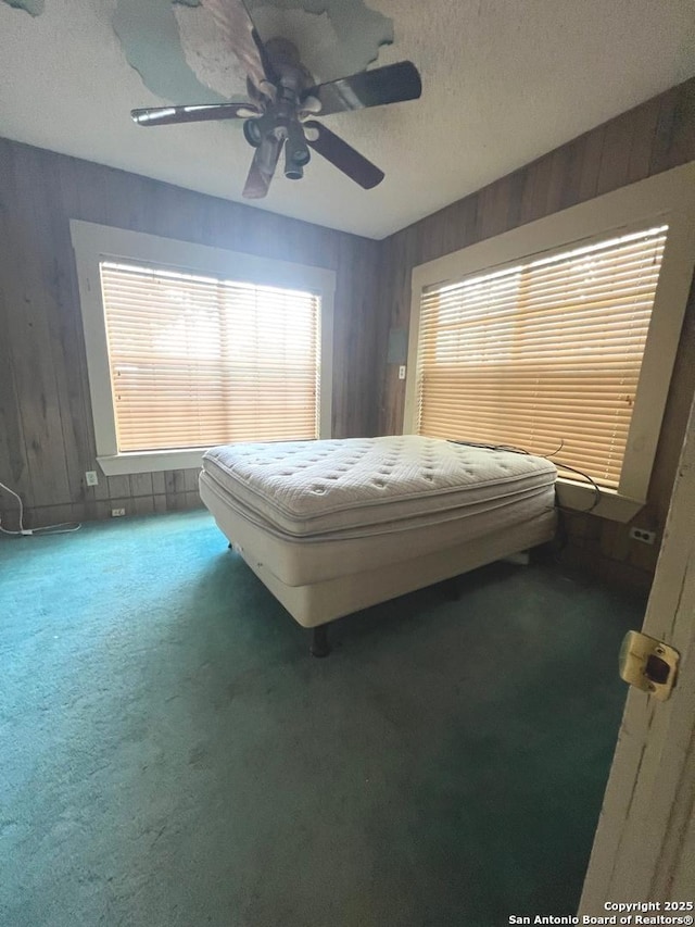 413 4th St, Poteet, TX 78065 - bedroom featuring carpet floors, multiple windows, wood walls, a ceiling fan, and a textured ceiling