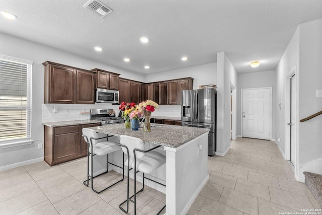 8919 Ladbroke, Converse, TX 78109 - kitchen featuring appliances with stainless steel finishes, tasteful backsplash, a kitchen island with sink, light stone countertops, and recessed lighting