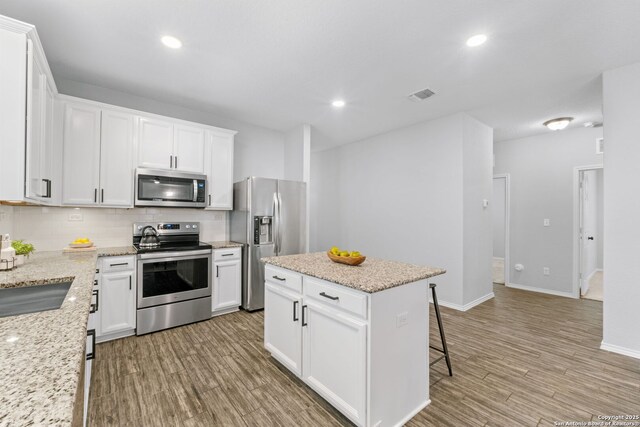 336 Salz, San Antonio, TX 78260 - kitchen featuring appliances with stainless steel finishes, decorative backsplash, light wood-type flooring, white cabinets, and a kitchen island