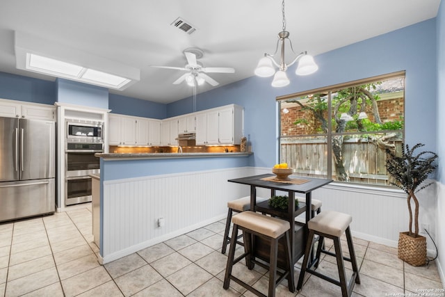 2430 Burning Trl, San Antonio, TX 78232 - kitchen with stainless steel appliances, a wainscoted wall, white cabinets, a peninsula, and light tile patterned floors