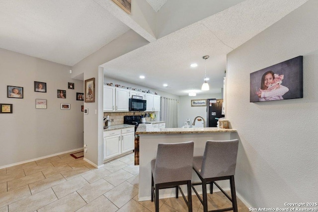 6411 Gray Rdg, San Antonio, TX 78233 - kitchen with black appliances, a textured ceiling, white cabinets, a kitchen bar, and a peninsula