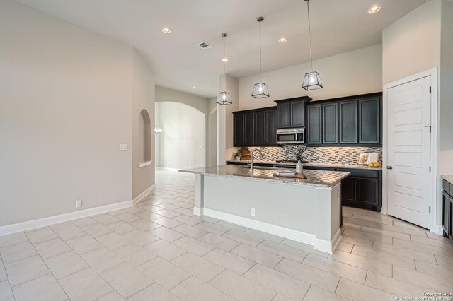 27123 Brook Bnd, Boerne, TX 78015 - kitchen with stainless steel microwave, arched walkways, tasteful backsplash, light stone counters, and a kitchen island with sink