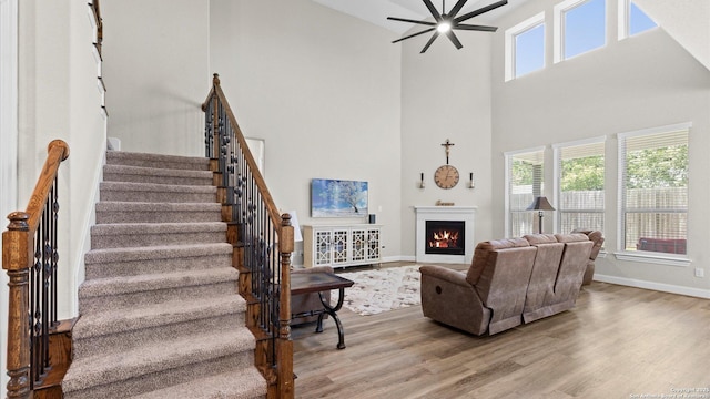 107 Destiny, Boerne, TX 78006 - living room featuring a towering ceiling, wood finished floors, a ceiling fan, stairway, and a warm lit fireplace