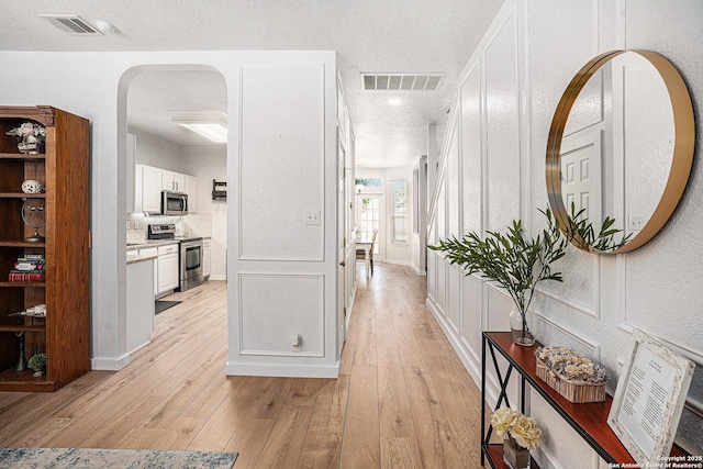 13812 Riverbank Pass, Helotes, TX 78023 - hallway featuring light wood-style floors, arched walkways, and a textured ceiling