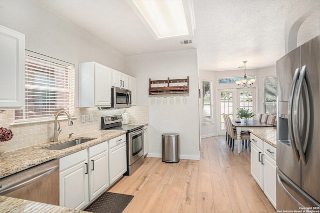 13812 Riverbank Pass, Helotes, TX 78023 - kitchen with appliances with stainless steel finishes, a chandelier, white cabinets, backsplash, and light stone counters