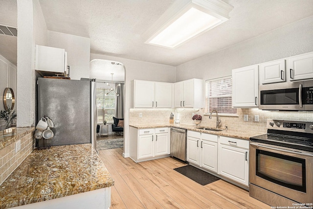 13812 Riverbank Pass, Helotes, TX 78023 - kitchen with stainless steel appliances, white cabinets, light wood-style floors, and tasteful backsplash