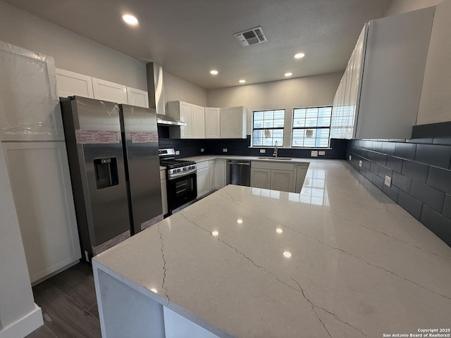 206 E Lambert, San Antonio, TX 78204 - kitchen featuring appliances with stainless steel finishes, light stone counters, wall chimney range hood, decorative backsplash, and a peninsula