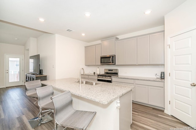 4951 Ranahan Pass, Saint Hedwig, TX 78152 - kitchen featuring appliances with stainless steel finishes, a center island with sink, light wood-type flooring, light stone counters, and gray cabinets