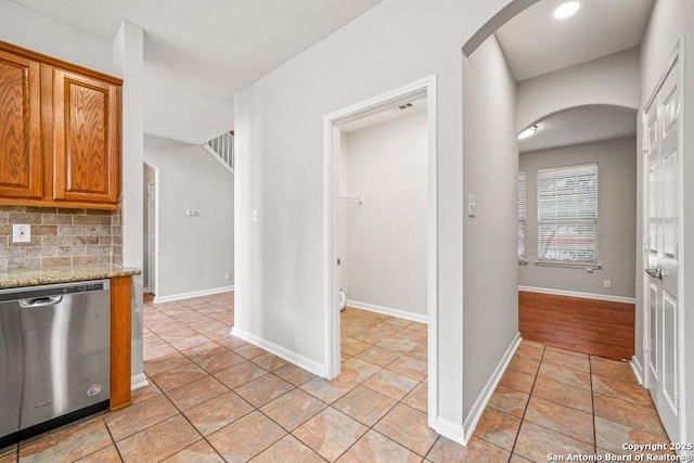 223 Verde Blf, San Antonio, TX 78258 - kitchen with stainless steel dishwasher, arched walkways, tasteful backsplash, brown cabinetry, and light stone countertops