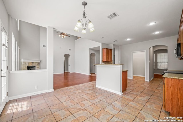 223 Verde Blf, San Antonio, TX 78258 - kitchen featuring arched walkways, a ceiling fan, a stone fireplace, brown cabinets, and light tile patterned floors
