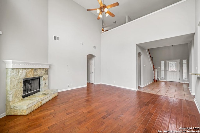 223 Verde Blf, San Antonio, TX 78258 - unfurnished living room featuring arched walkways, a ceiling fan, hardwood / wood-style floors, a high ceiling, and a stone fireplace