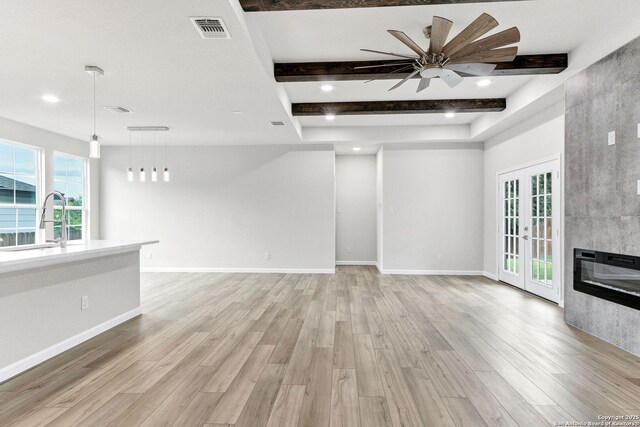 9911 Loma Alta Cir, Converse, TX 78109 - unfurnished living room with light wood-type flooring, beamed ceiling, ceiling fan, a fireplace, and french doors