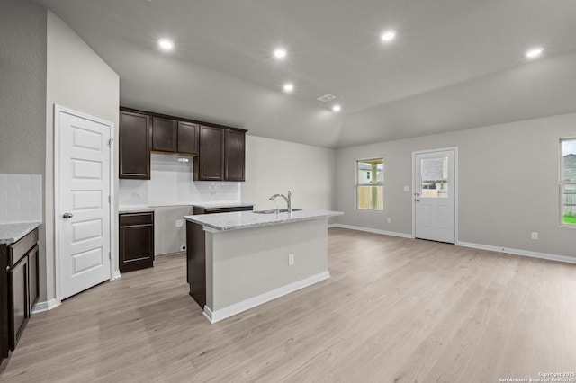 13519 Beebrush Saddle, San Antonio, TX 78253 - kitchen with dark brown cabinetry, backsplash, light wood-style flooring, a kitchen island with sink, and vaulted ceiling
