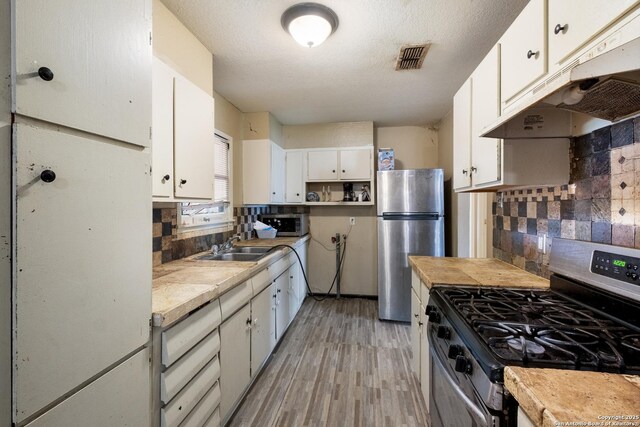 503 E Palfrey, San Antonio, TX 78223 - kitchen with stainless steel appliances, under cabinet range hood, light countertops, light wood finished floors, and white cabinets
