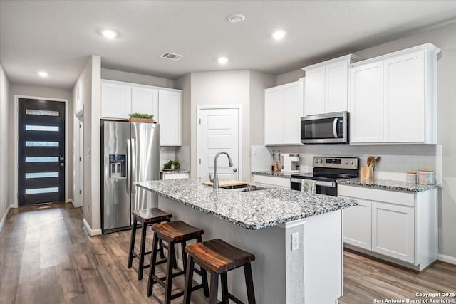 3016 Muscat, Schertz, TX 78154 - kitchen featuring appliances with stainless steel finishes, wood finished floors, an island with sink, decorative backsplash, and a kitchen breakfast bar