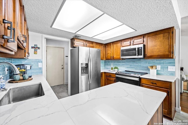 3527 Oakhorne St, San Antonio, TX 78247 - kitchen featuring stainless steel appliances, a textured ceiling, brown cabinetry, decorative backsplash, and a peninsula