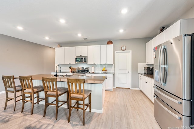 13215 Turnesa Ter, San Antonio, TX 78221 - kitchen with appliances with stainless steel finishes, a kitchen bar, light wood finished floors, a center island with sink, and white cabinetry
