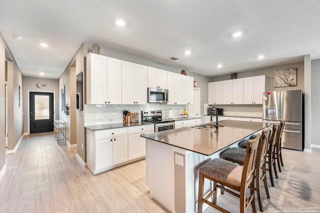 13215 Turnesa Ter, San Antonio, TX 78221 - kitchen with appliances with stainless steel finishes, a breakfast bar, light wood finished floors, white cabinets, and recessed lighting