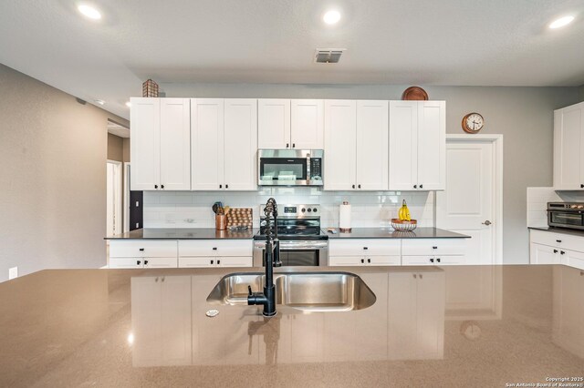 13215 Turnesa Ter, San Antonio, TX 78221 - kitchen with stainless steel appliances, decorative backsplash, dark countertops, white cabinetry, and recessed lighting