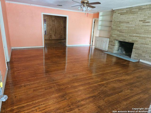 2310 W Gramercy, San Antonio, TX 78201 - unfurnished living room with ornamental molding, ceiling fan, wood finished floors, and a brick fireplace