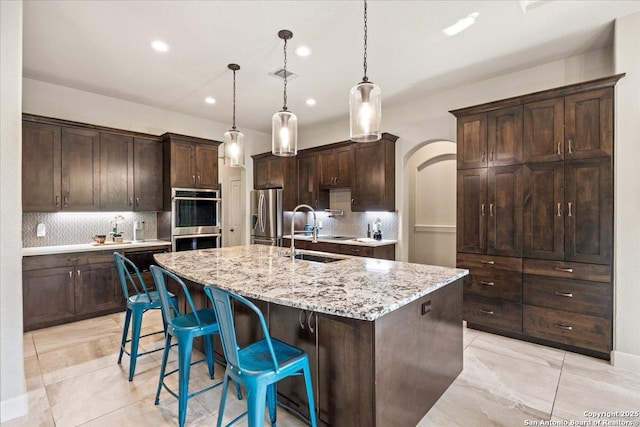 26815 Duet Dr, San Antonio, TX 78260 - kitchen featuring appliances with stainless steel finishes, recessed lighting, tasteful backsplash, dark brown cabinets, and a kitchen island with sink