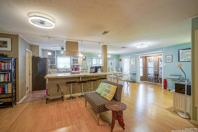9518 Wahada, San Antonio, TX 78217 - kitchen with freestanding refrigerator, a textured ceiling, light wood finished floors, a kitchen breakfast bar, and a peninsula