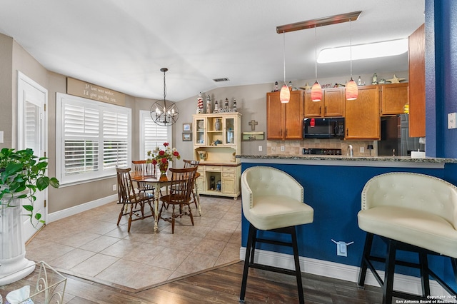 5330 Stormy Hls, San Antonio, TX 78247 - kitchen with freestanding refrigerator, black microwave, a chandelier, brown cabinets, and hanging light fixtures