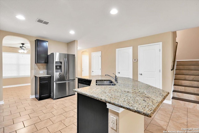 14055 Cremello Fls, San Antonio, TX 78254 - kitchen featuring appliances with stainless steel finishes, arched walkways, ceiling fan, a kitchen island with sink, and light stone counters