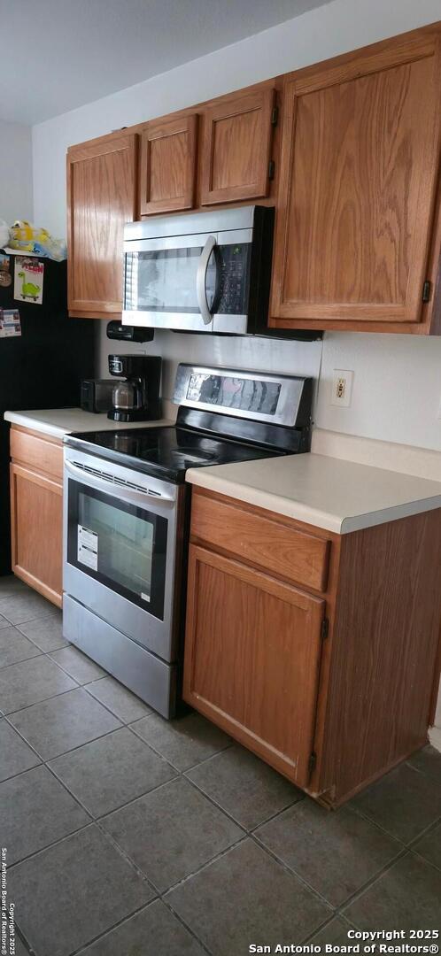 335 Silver Bit, San Antonio, TX 78227 - kitchen featuring appliances with stainless steel finishes, dark tile patterned flooring, light countertops, and brown cabinetry