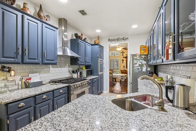 8526 Spartan Ter, Universal City, TX 78148 - kitchen featuring wall chimney range hood, appliances with stainless steel finishes, blue cabinetry, light stone counters, and tasteful backsplash
