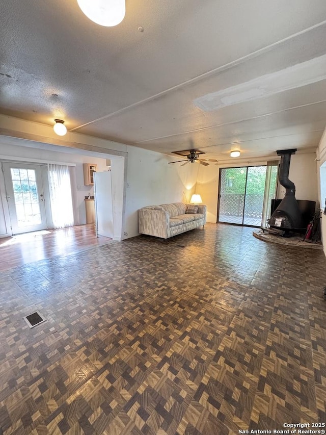 323 N Scenic Loop, Canyon Lake, TX 78133 - unfurnished living room featuring a wood stove, healthy amount of natural light, a textured ceiling, a ceiling fan, and french doors