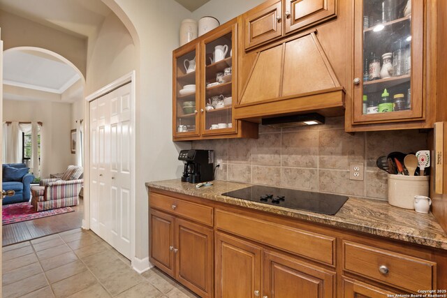 7 Mcinnis, Bulverde, TX 78163 - kitchen featuring black electric cooktop, custom exhaust hood, arched walkways, brown cabinetry, and ornamental molding