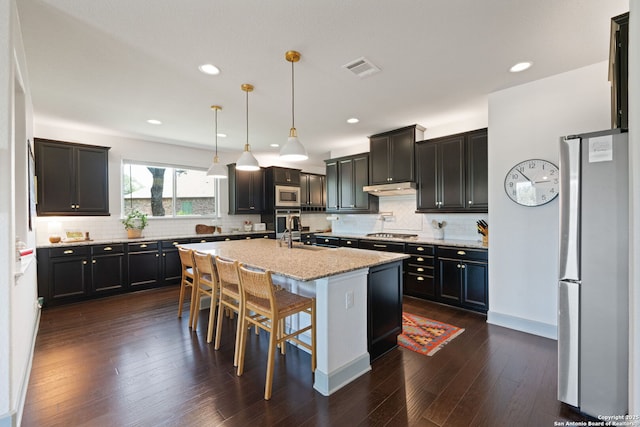 8903 Gate Pass, Boerne, TX 78015 - kitchen featuring appliances with stainless steel finishes, backsplash, a kitchen island with sink, light stone countertops, and recessed lighting