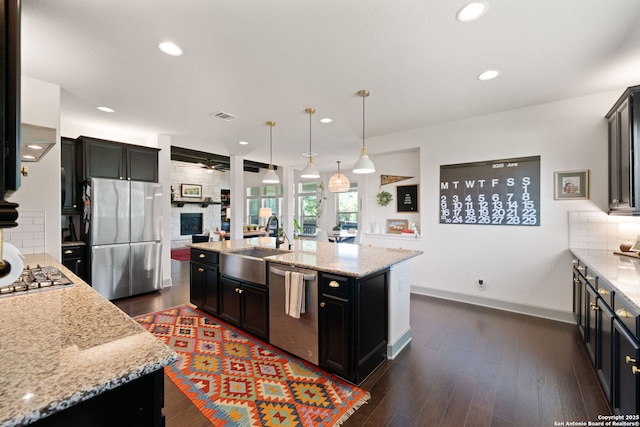 8903 Gate Pass, Boerne, TX 78015 - kitchen with appliances with stainless steel finishes, decorative backsplash, light stone countertops, a kitchen island with sink, and dark wood-style flooring