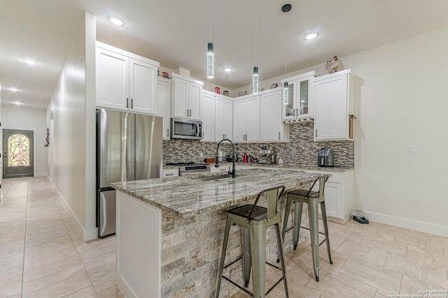 114 Mokukua Ln, Bastrop, TX 78602 - kitchen with stainless steel appliances, tasteful backsplash, light stone counters, a kitchen breakfast bar, and a center island with sink