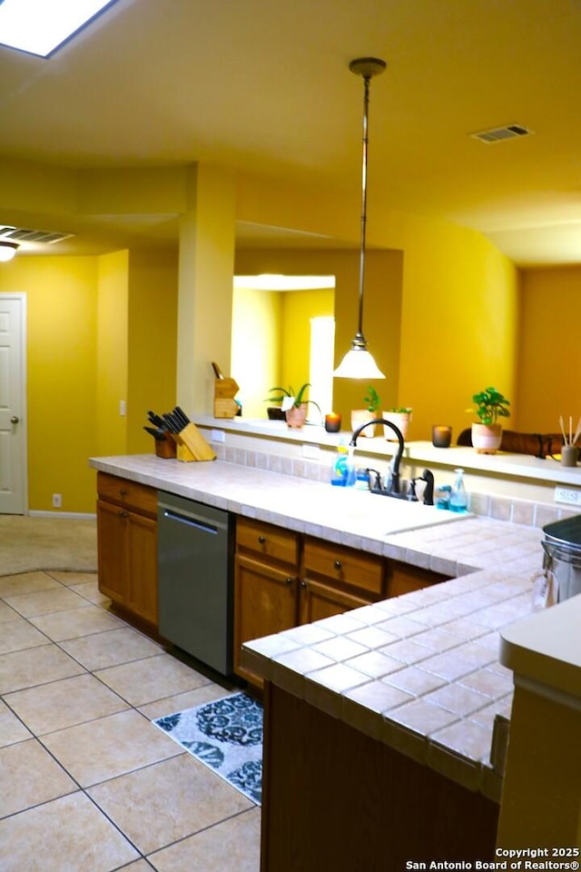 9522 Sage Ter, San Antonio, TX 78251 - kitchen with dishwasher, tile counters, light tile patterned floors, hanging light fixtures, and brown cabinetry