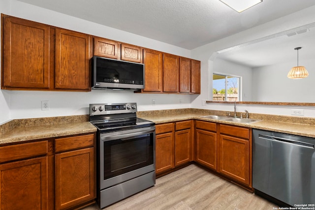221 Passerina Spur, Schertz, TX 78154 - kitchen featuring appliances with stainless steel finishes, light wood finished floors, hanging light fixtures, and brown cabinets
