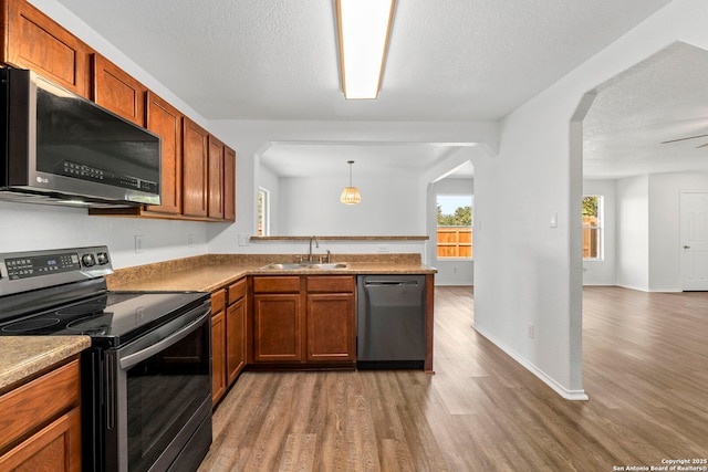 221 Passerina Spur, Schertz, TX 78154 - kitchen featuring appliances with stainless steel finishes, light wood-style flooring, a peninsula, brown cabinets, and a textured ceiling