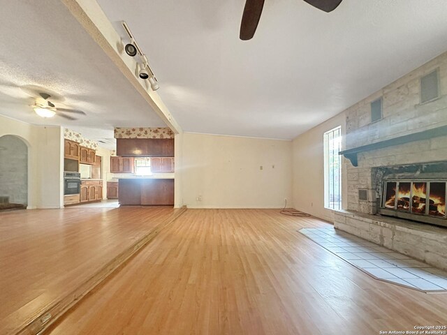 3923 Maxine, San Antonio, TX 78228 - unfurnished living room featuring ceiling fan, a stone fireplace, light wood-type flooring, and arched walkways